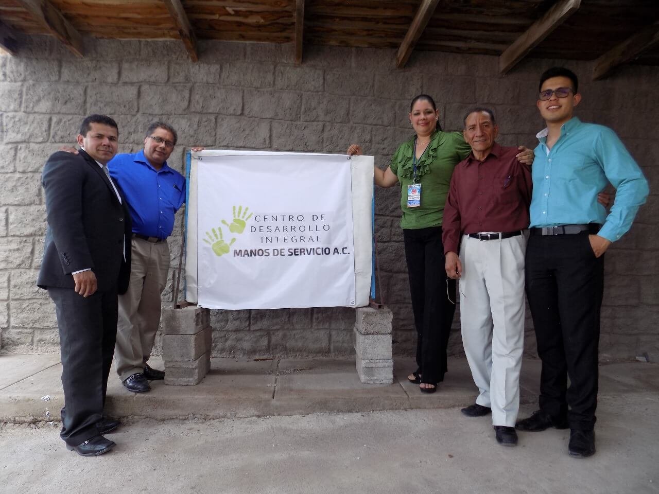 Equipo de Manos de Servicio A.C. posando con su estandarte en las instalaciones.